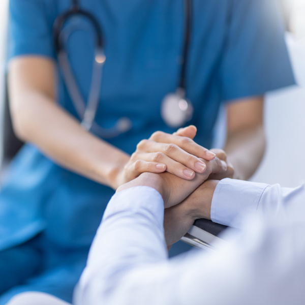 Nahaufnahme einer Ärztin in blauer Uniform mit Stethoskop, die die Hand eines Patienten hält.