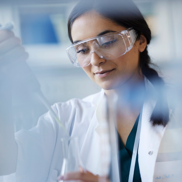 Wissenschaftlerin mit Kittel und Schutzbrille im Labor arbeitet mit einer Pipette.