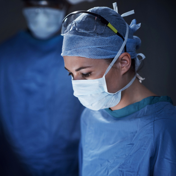 Ärztin im OP-Saal mit OP-Kittel, Mundschutz und Schutzbrille.