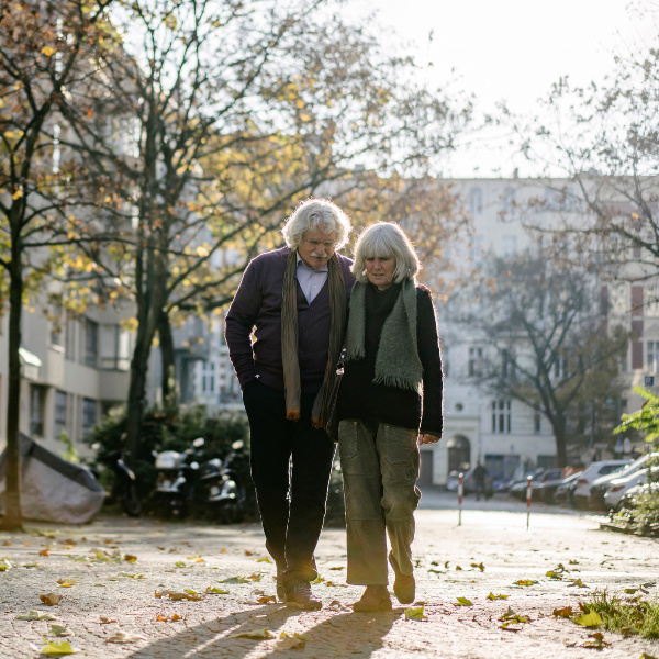 Ein älteres Paar spaziert Hand in Hand durch herbstliche Stadtstraße.