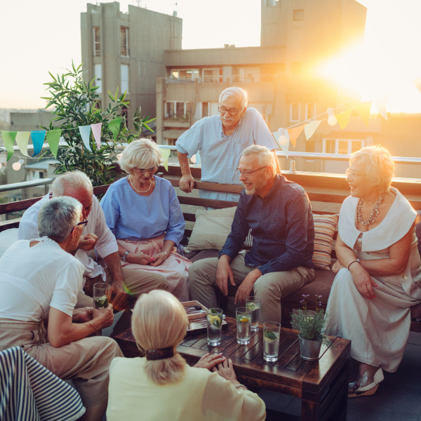 Eine Gruppe von Senioren, die auf einer Terrasse bei Sonnenuntergang zusammensitzen und sich am Tisch unterhalten.