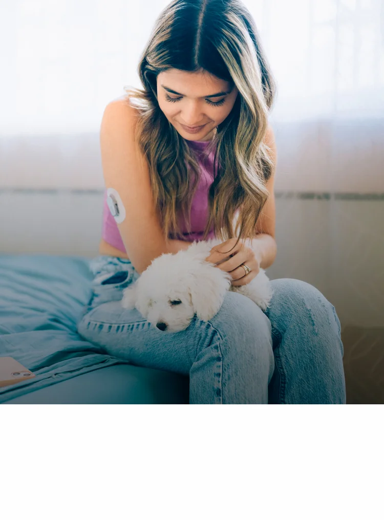 Ein Mädchen mit Typ-1 Diabetes sitzt mit einem Hund auf dem Schoß auf einem Bett Ein Mädchen mit Typ-1 Diabetes sitzt mit einem Hund auf dem Schoß auf einem Bett